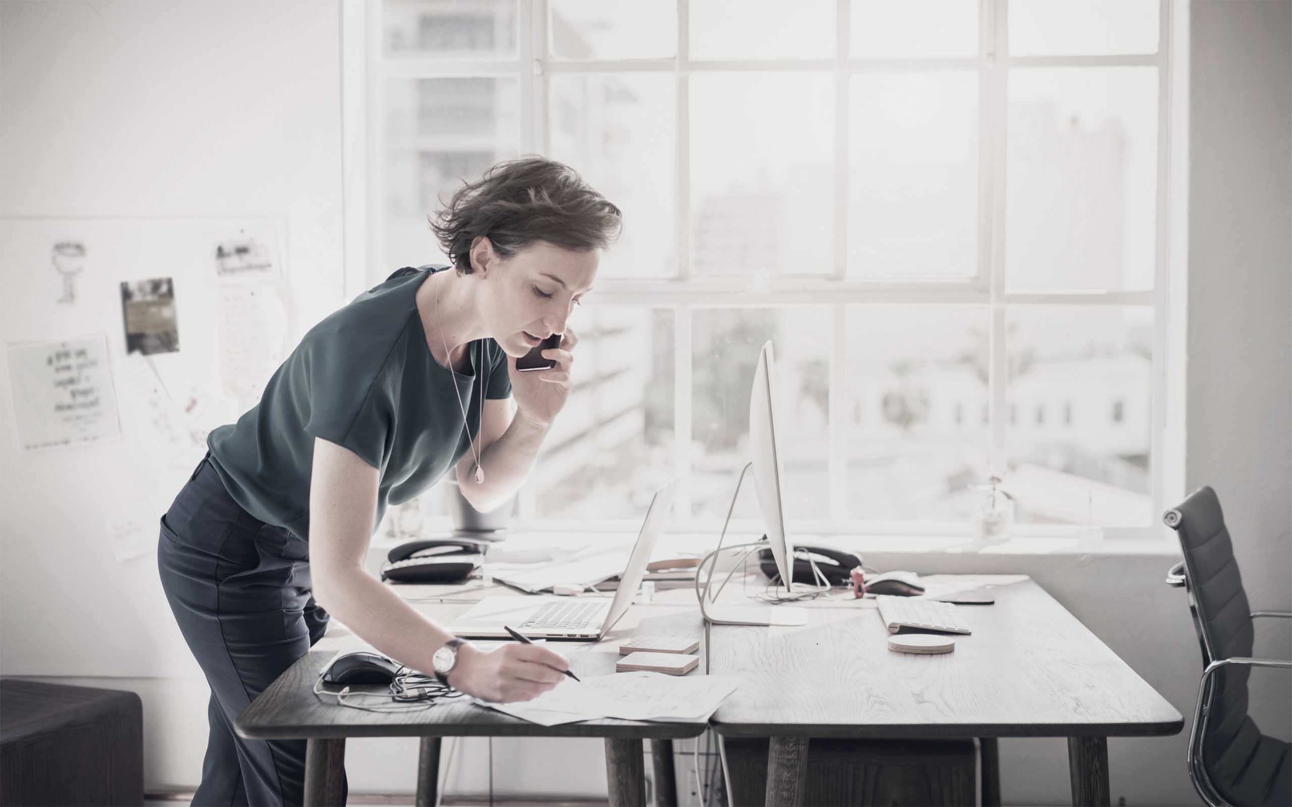 geschäftsfrau-steht-an-einem-tisch-in-einem-loft-telefoniert-und-macht-sich-notizen.jpg